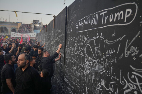 Mourners write messages on a wall, including one in English that reads "We will kill Trump," during the funeral ceremonies for slain Iranian Supreme Leader Ayatollah Ali Khamenei and members of his family at the Imam Khomeini Mosalla Grand Mosque in Tehran, Iran, Saturday, July 4, 2026. (AP Photo/Altaf Qadri)