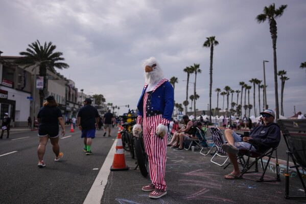 Brian White, dressed in a bald eagle costume and patriotic U.S. flag-based clothing, stands along the route of an Independence Day parade in Huntington Beach, Calif., Saturday, July 4, 2026. (AP Photo/Jae C. Hong)