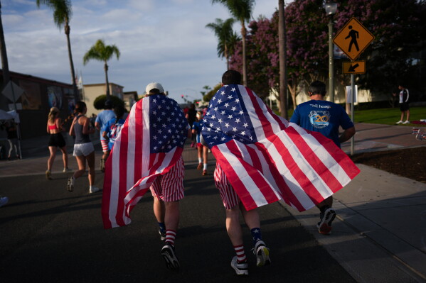 Runners draped in American flags participate in a run on Independence Day in Huntington Beach, Calif., Saturday, July 4, 2026. (AP Photo/Jae C. Hong)
