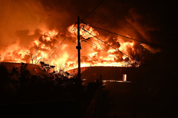 Blazes rise from a burning building during a wildfire on the outskirts of the northern city of Thessaloniki, Greece, early Sunday, July 5, 2026. (AP Photo/Giannis Papanikos)