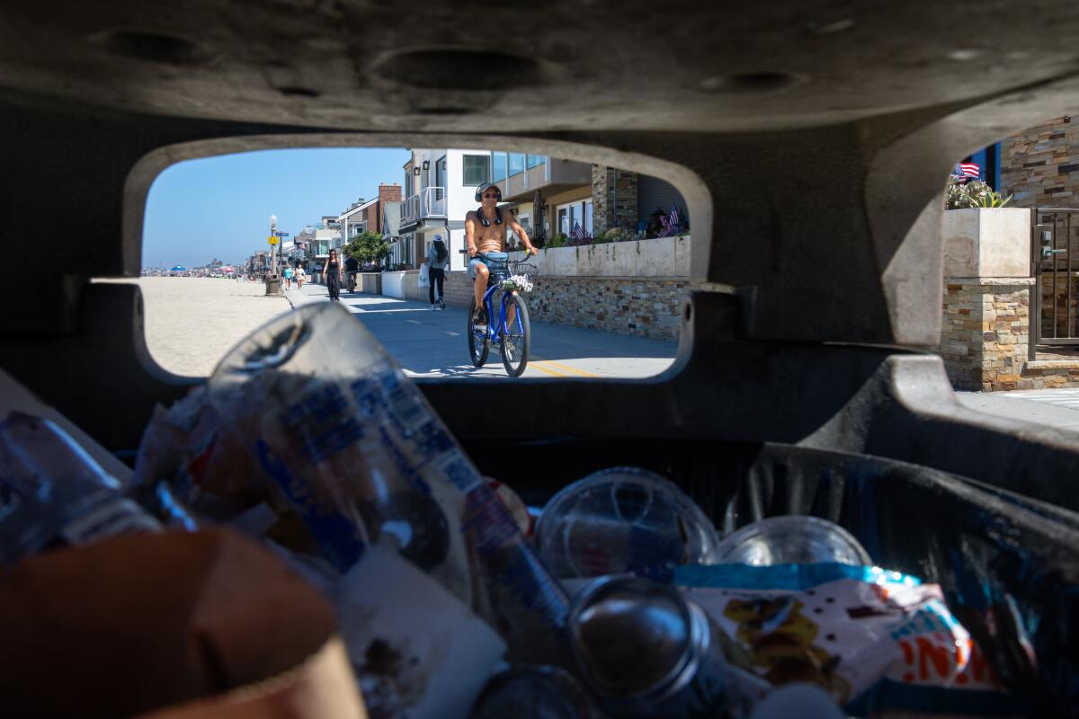 A biker rides past a full trash can along W. Ocean Front boardwalk in Newport Beach.