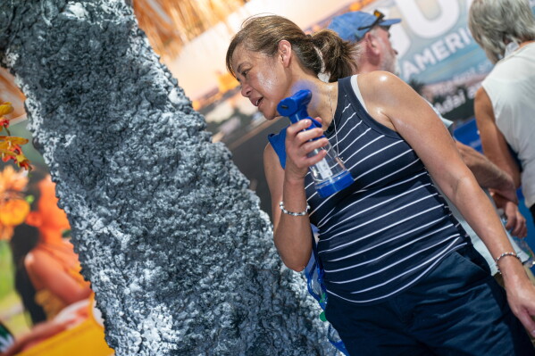 A visitor to the Guam tent uses a fan to cool down while attending the Great American State Fair on the National Mall, July 1, 2026, in Washington. (AP Photo/Nathan Howard, File)