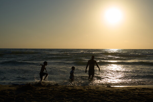 A family enjoys part of the Mediterranean Sea that is near a military firing range that is slated to be cleared in Rishon LeZion on Tuesday, June 23, 2026. (AP Photo/Ariel Schalit)
