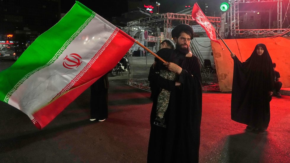 A cleric waves an Iranian flag while holding a child as a woman waves a religious flag in a...