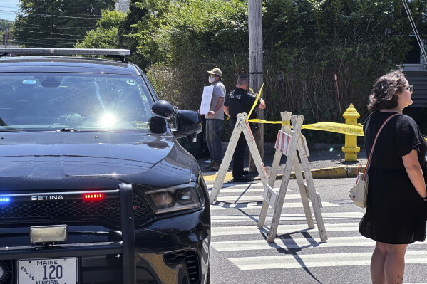 People stand near the scene as police block a road after a shooting involving U.S. Immigration and Customs Enforcement, in Biddeford, Maine, Monday, July 13, 2026. (AP Photo/Patrick Whittle)