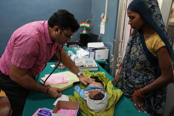 Dr. Abhishek Pranayami examines a child suffering from a heat-related illness amid high temperatures as the child's mother looks on at a government hospital during a heat wave Banda, northern Indian state of Utter Pradesh, Friday, June 19 , 2026. (AP Photo/Rajesh Kumar Singh)
