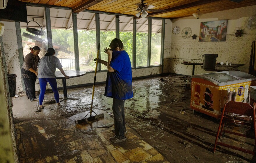 People move furniture and sweep mud out of a building which is wet and muddy from flood waters.