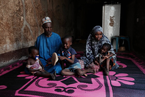 Shehu Aminu, second left, who lost his job as a taxi driver due to a spike in the retail price of petrol in February, sits with his wife Maryam Aminu, their daughter Farisa, left, who has relapsed into malnutrition, and her siblings, at their house in Kware Sokoto, northwestern Nigeria, Wednesday, July 15, 2026. (AP Photo/Sunday Alamba)