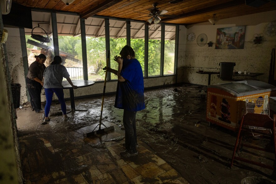 People move furniture and clean inside of a flooded room layered with mud and dirt.