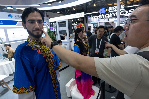 A man reacts after touching the face of a lifelike robot head depicting a ethnic minority on display from Yunmu Intelligence Manufacturing during the World AI Conference in Shanghai, Friday, July 17, 2026. (AP Photo/Ng Han Guan)