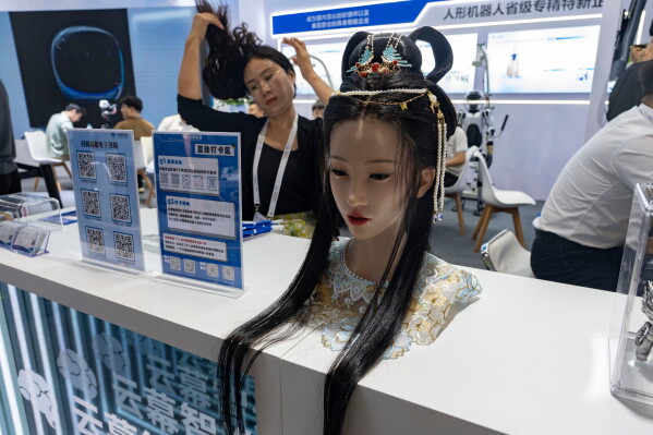 A woman adjusts her hair near a lifelike robot head on display from Yunmu Intelligence Manufacturing during the World AI Conference in Shanghai, Friday, July 17, 2026. (AP Photo/Ng Han Guan)
