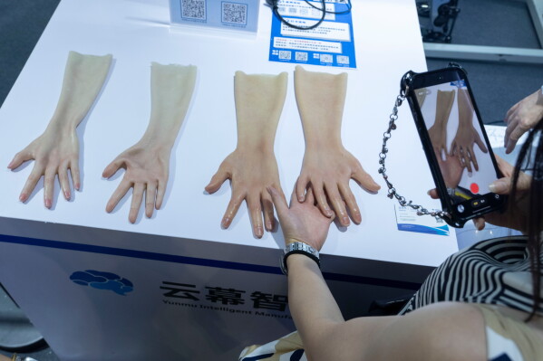 A woman takes photos of realistic skin for robotic hands on display from Yunmu Intelligence Manufacturing during the World AI Conference in Shanghai, Friday, July 17, 2026. (AP Photo/Ng Han Guan)