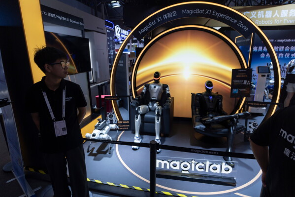 A worker looks on near humanoid robots on display from Magiclab, a Chinese embodied AI and humanoid robots company during the World AI Conference in Shanghai, Saturday, July 18, 2026. (AP Photo/Ng Han Guan)
