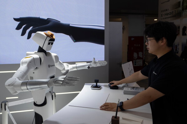 A worker prepares a robot to demonstrate the performances of its hands at the booth for Chinese company Xynova during the World AI Conference in Shanghai, Saturday, July 18, 2026. (AP Photo/Ng Han Guan)