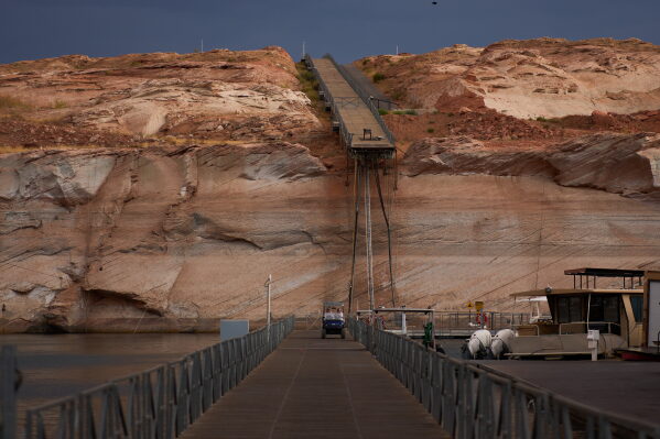 People ride a golf cart beneath a protruding dock used during higher water levels at the Antelope Point Marina on Lake Powell at the Glen Canyon National Recreation Area, Tuesday, July 14, 2026, near Page, Ariz. (AP Photo/John Locher)