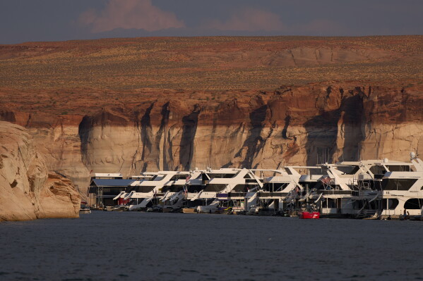 Houseboats are moored at the Antelope Point Marina on Lake Powell at the Glen Canyon National Recreation Area, Wednesday, July 15, 2026, near Page, Ariz. A bathtub ring of light minerals on the canyon walls show the high water mark of the reservoir. (AP Photo/John Locher)