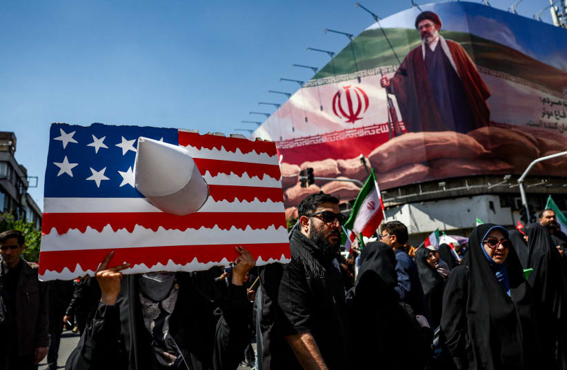 A person holds a placard representing a US flag, with an image of Iran's new Supreme Leader Mojtaba Khamenei on a billboard in the background, on the day of a ceremony marking 40 days since Ayatollah Ali Khamenei was killed, in Tehran, Iran, April 9, 2026.
