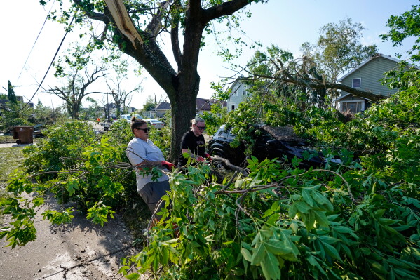 Cassandra Baron, left, and Brooke Baron pull fallen tree branches off of a car after a tornado struck Monday, July 27, 2026, in Menasha, Wis. (AP Photo/Kayla Wolf)