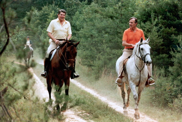 In this July 1981 file photo released by The White House, U.S. President Ronald Reagan, left, and Vice President George Bush go horseback riding at Camp David, Md. (Michael Evans/The White House, via AP, File)