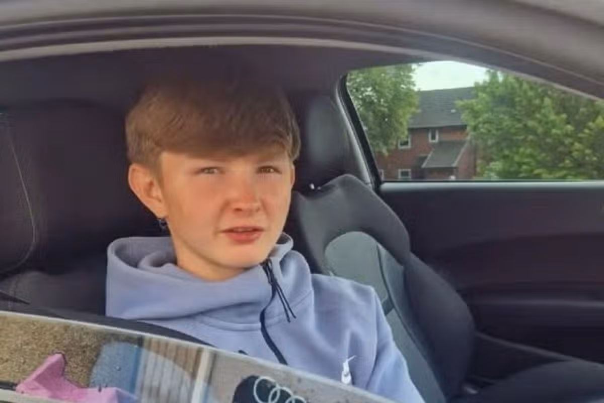 A young-looking white, teenage boy in a blue top sat in a car