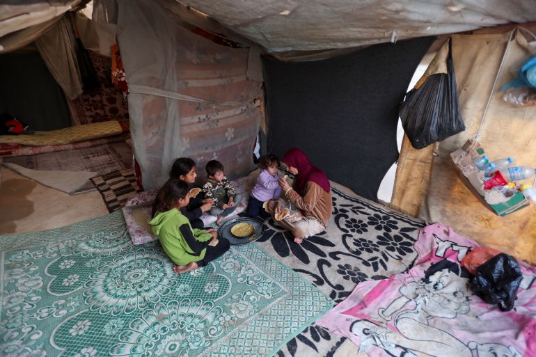 A displaced Palestinian mother has a meal with her children inside a tent in Deir el-Balah. The war has led to malnutrition and psychological strain, which has taken a particular toll on pregnant women