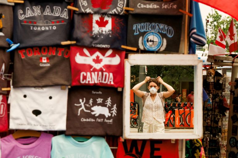 A person puts on a mask as reflected in a souvenir shop mirror, as wildfire smoke from northwestern Ontario fills the sky, in Toronto on Wednesday