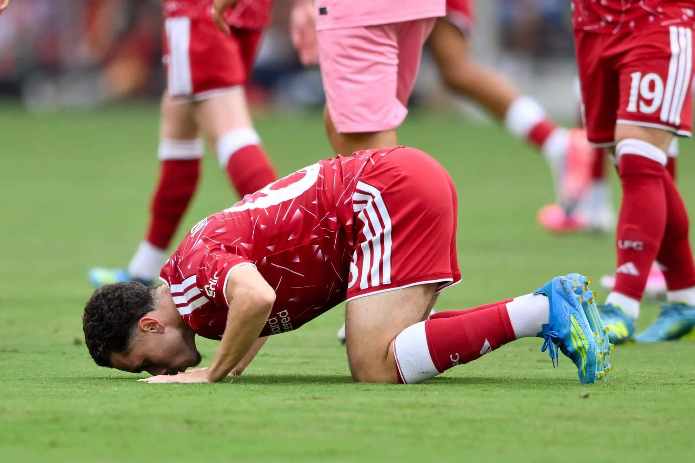 A footballer in a red shirt kisses the grass