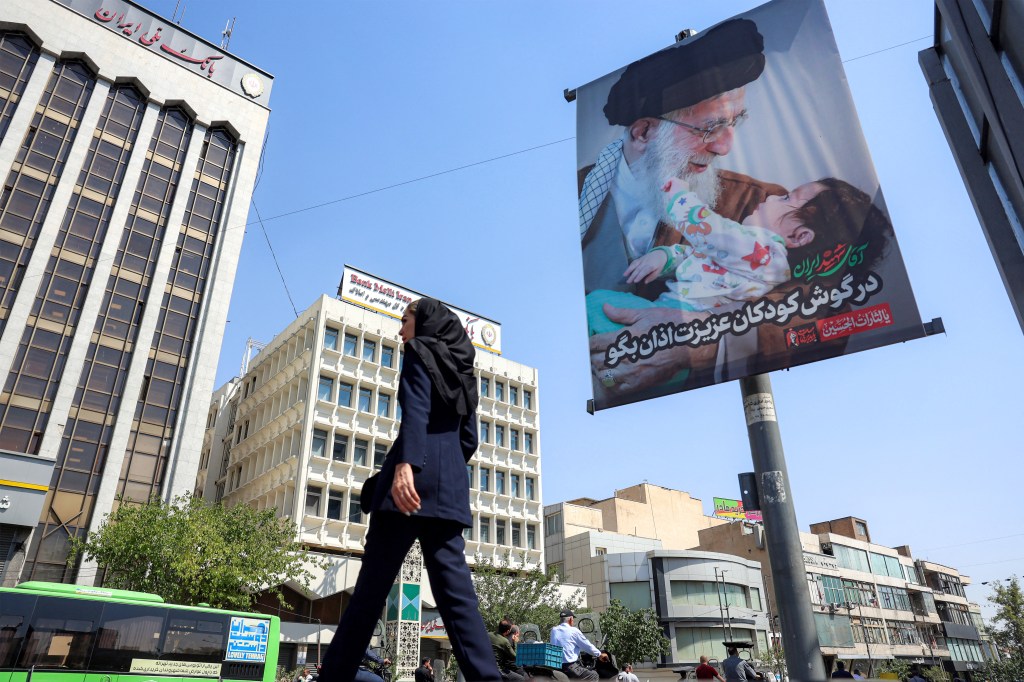 A woman walks past a billboard depicting Iran's slain supreme leader Ali Khamenei holding a child.