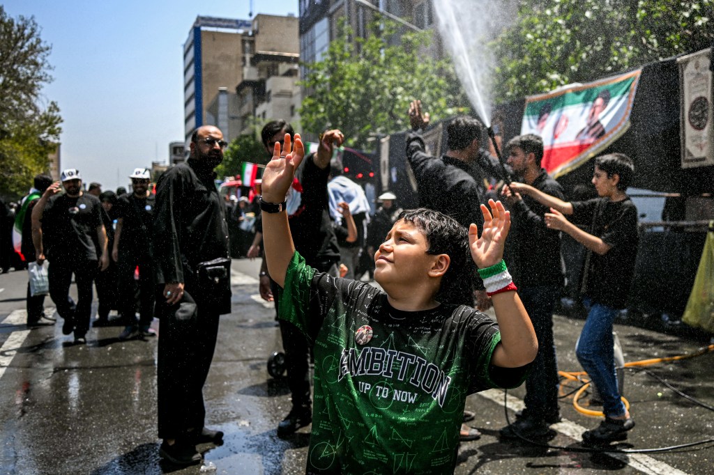 A boy is sprayed with water to cool off during a funeral ceremony in Tehran.