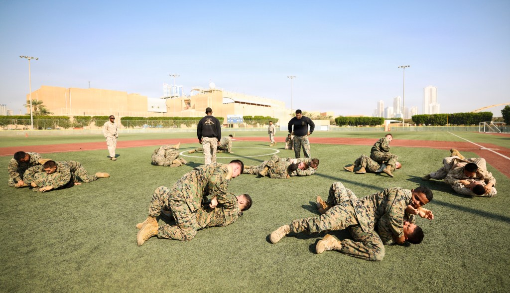 U.S. Marines practice combat maneuvers on a green field.