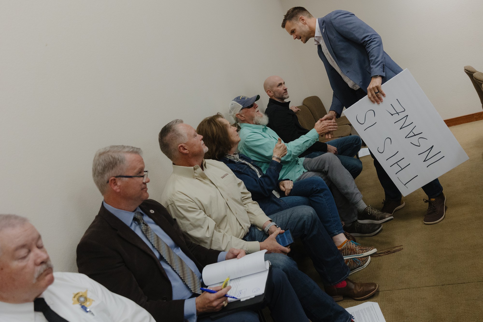 Matt Long shakes hands with attendees while holding a sign that says “This is insane” of a Hood County Commissioners Court meeting in Granbury on February 23, 2026. The pause would allow for the county to assess water and power usage of the proposed eight data centers that would be built in the county.