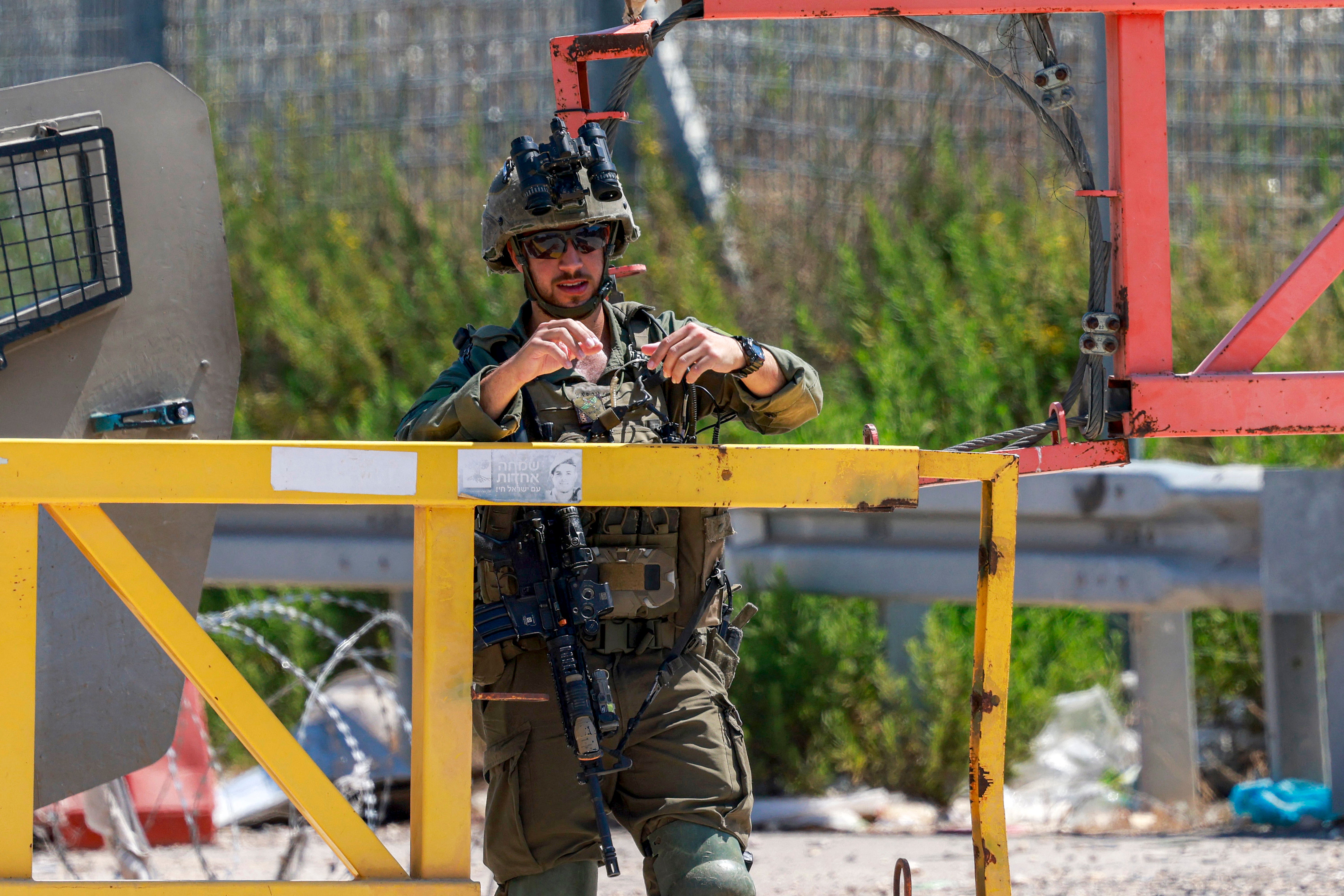 An Israeli soldier stands guard while people from the Palestinian town of Azzun, east of Qalqilya in the occupied West Bank, gather by the vehicle barrier at the entrance of the town on July 12, 2026
