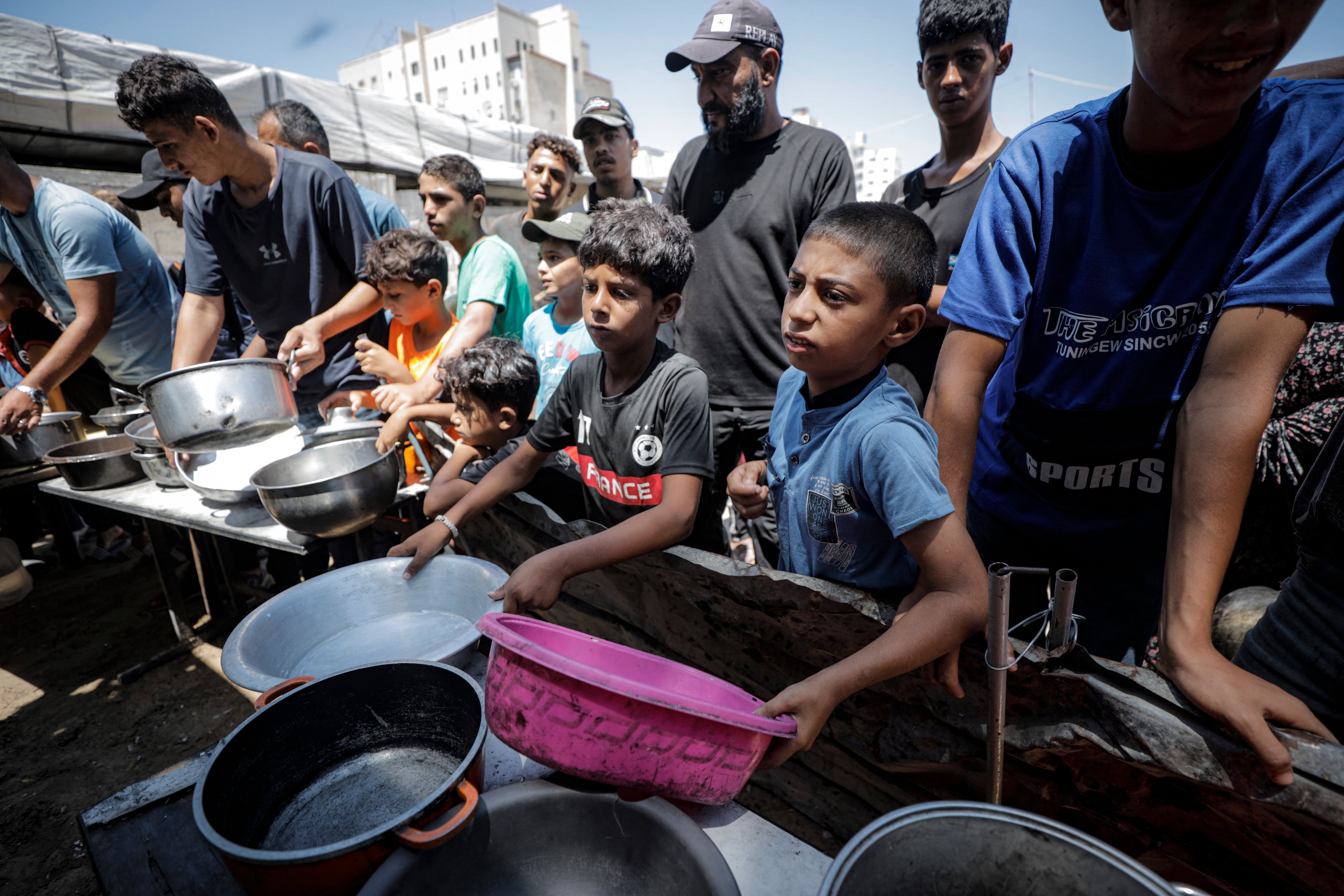 Displaced Palestinians hold empty pots and containers to receive food supplies in Gaza City, Gaza Strip, on July 27, 2026. Widespread displacement and the ongoing conflict have severely disrupted access to essential resources, leaving many families reliant on communal relief efforts for their daily meals