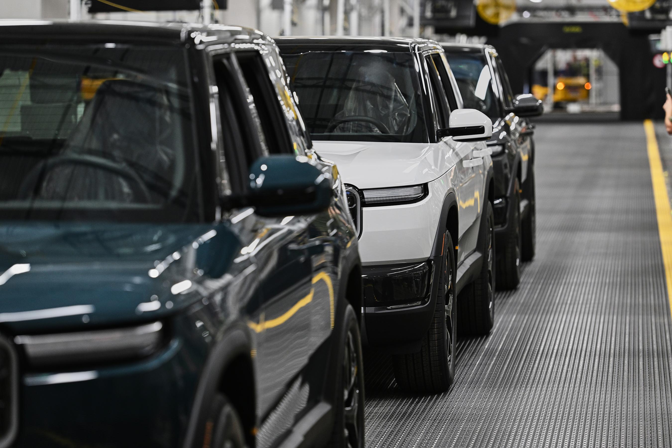 Detail of the sides of three Rivians in a line on the factory floor.