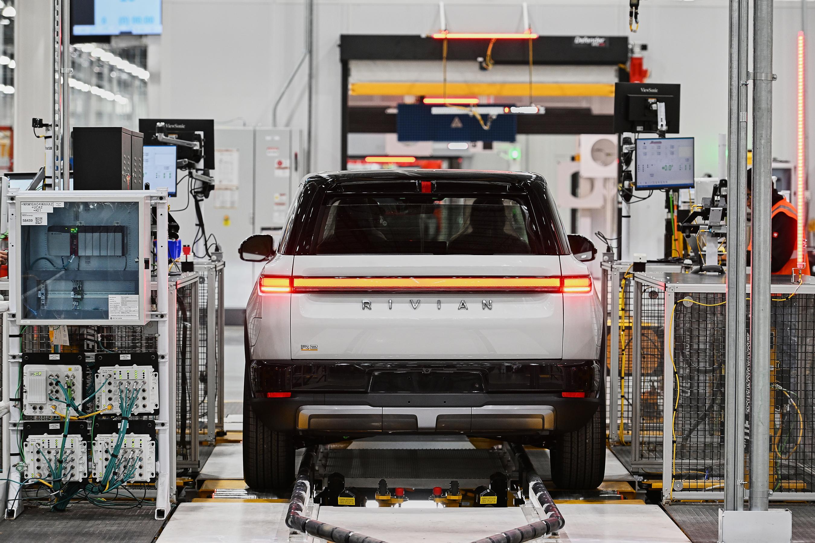 A white Rivian in between computer equipment seen from behind at the factory.