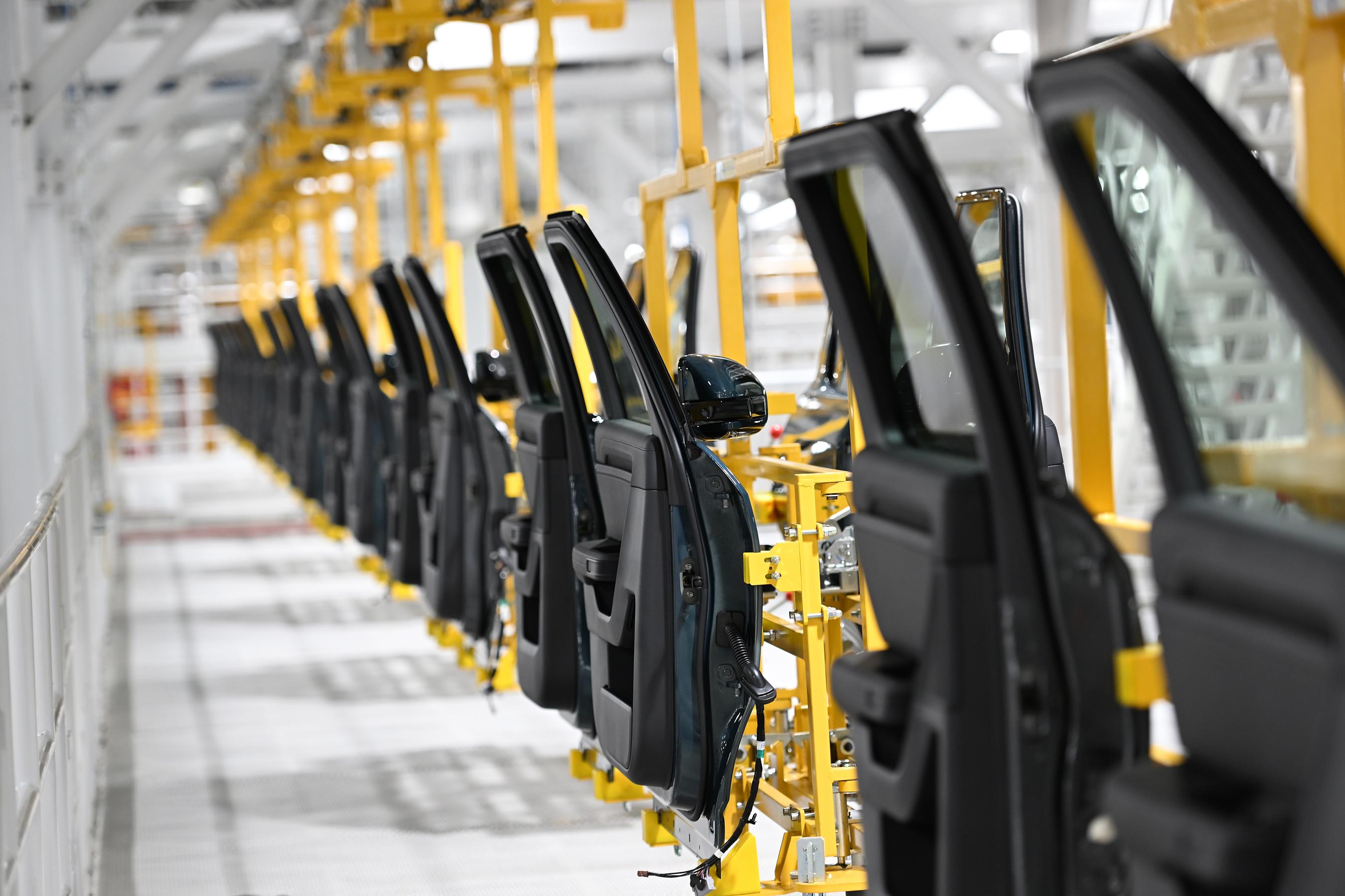 A long line of car doors are suspended along the edge of the Rivian Factory.