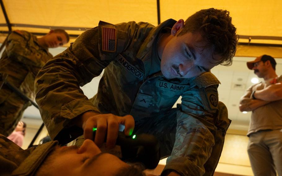 A soldier uses a handheld device to examine another soldier lying down.