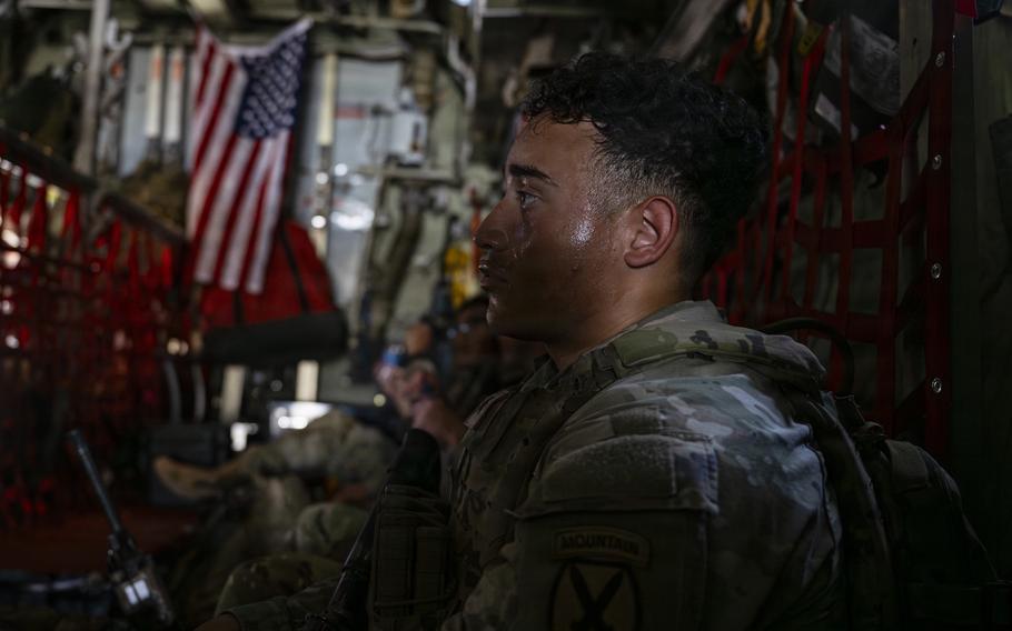 Soldiers sit along the interior wall of a military cargo plane.