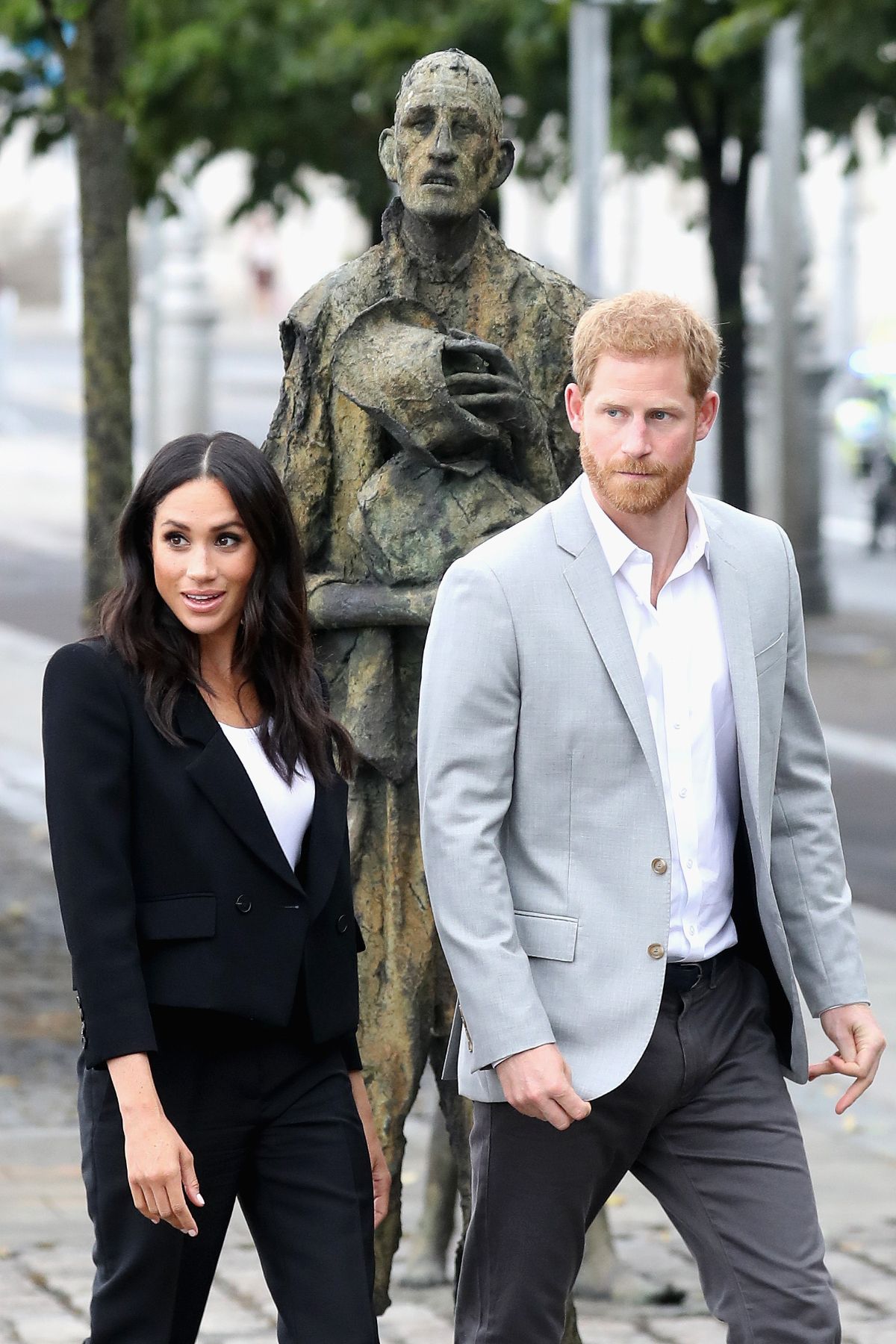 Meghan Markle and Prince Harry walk alongside each other in front of a statue