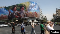 People walk past a billboard depicting the founder of the Islamic republic and its first supreme leader, Ayatollah Ruhollah Khomeini, and his successor, Ayatollah Ali Khamenei, on a street in Tehran on June 6.