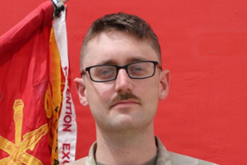 A close-up of a young man with glasses and a moustache