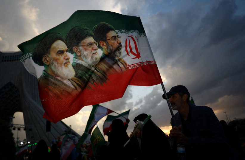 A MAN holds a flag with a picture of late leader of the Islamic Revolution Ayatollah Ruhollah Khomeini, late supreme leader Ayatollah Ali Khamenei, and Iran’s new Supreme Leader Mojtaba Khamenei, during a rally in Tehran, in April 2026.