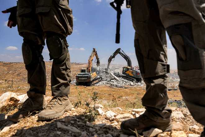 TOPSHOT-PALESTINIAN-ISRAEL-CONFLICT-WEST BANK-DEMOLITION TOPSHOT - Israeli security forces stand guard as their excavators demolish a Palestinian home which Israeli authorities say was built without permission in the village of al-Rifayia, south of Hebron in the occupied West Bank, on July 7, 2026. (Photo by HAZEM BADER / AFP via Getty Images)
