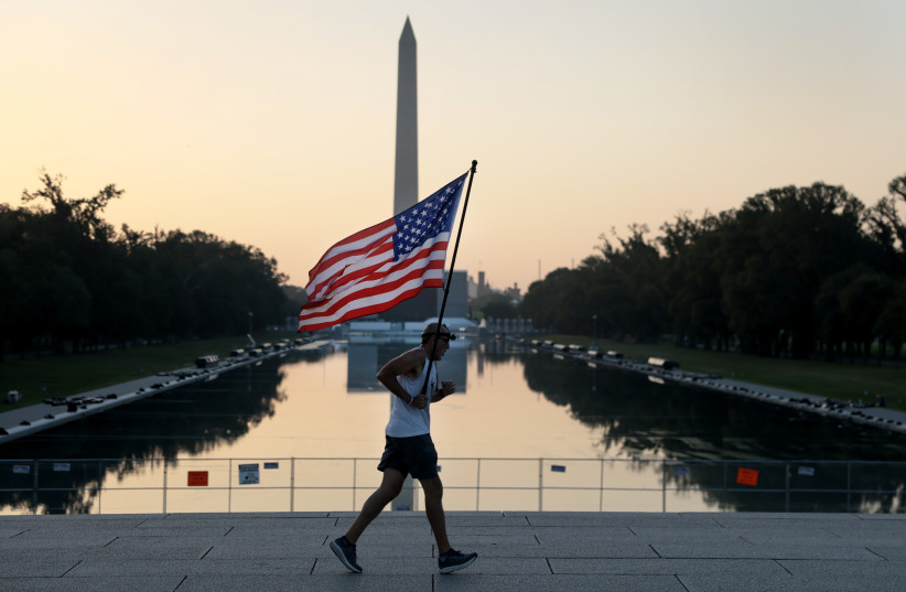 Pete Folch carries an American flag during a morning run past the Reflecting Pool as the city prepares for July 4th festivities on July 03, 2026, in Washington, DC.