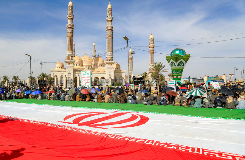 Men gather alongside a giant unfurled Iranian flag, as supporters of the Iranian-backed Huthi movement gather at a mass rally, denouncing what they perceive to be derogatory comments by the US president regarding the holy city, in Yemen's Huthi-held capital Sanaa on June 16, 2026