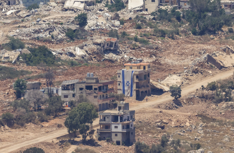 A man walks past an Israeli flag covering part of a destroyed building in the southern Lebanese village of Taybeh, near the border, on June 18.