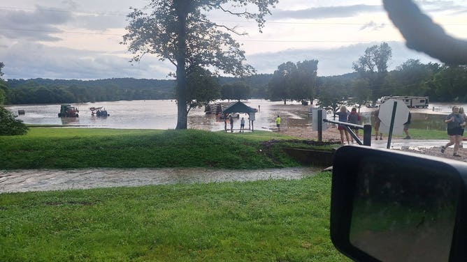 Several people stand around a campground site near Black River in Lesterville, MO, which is badly flooded.