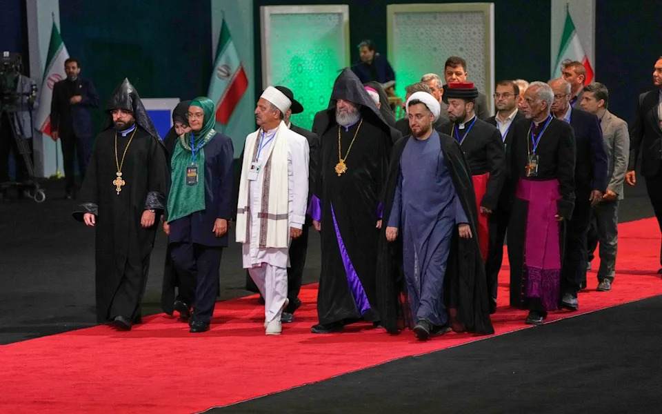 Iranian religious leaders and other mourners walk past the coffins during a viewing ceremony on Friday