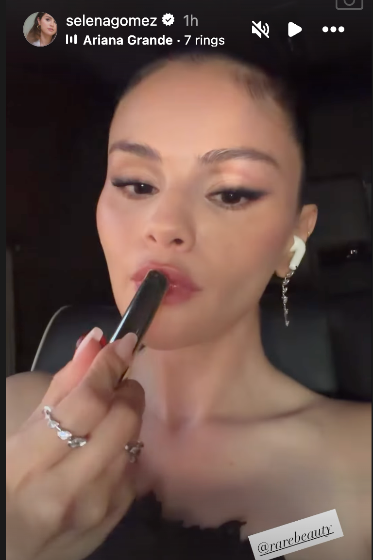 A person applying lipstick while wearing earrings and AirPods, with a dark background. A person applying lipstick while wearing earrings and AirPods, with a dark background.