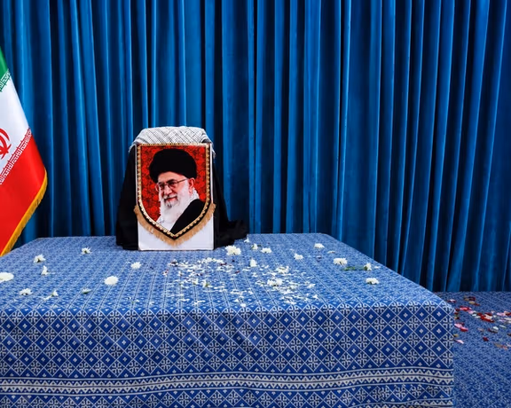 A portrait of Iran's Supreme Leader Ali Khamenei is displayed on a black-draped ceremonial stand adorned with a mourning banner.